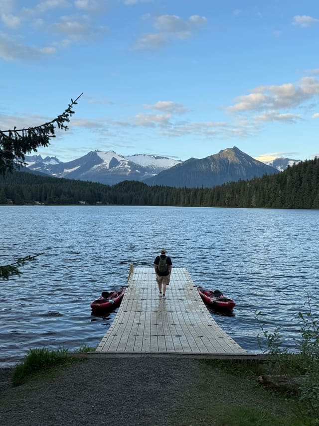 A student walking out onto the dock at Auke Lake, mountains behind